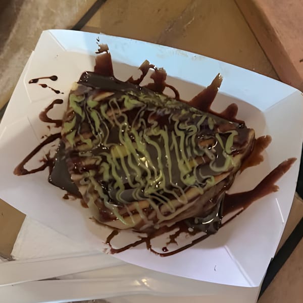 A Halal Fusionz crepe drizzled with chocolate and green pistachio sauces in a white paper tray.