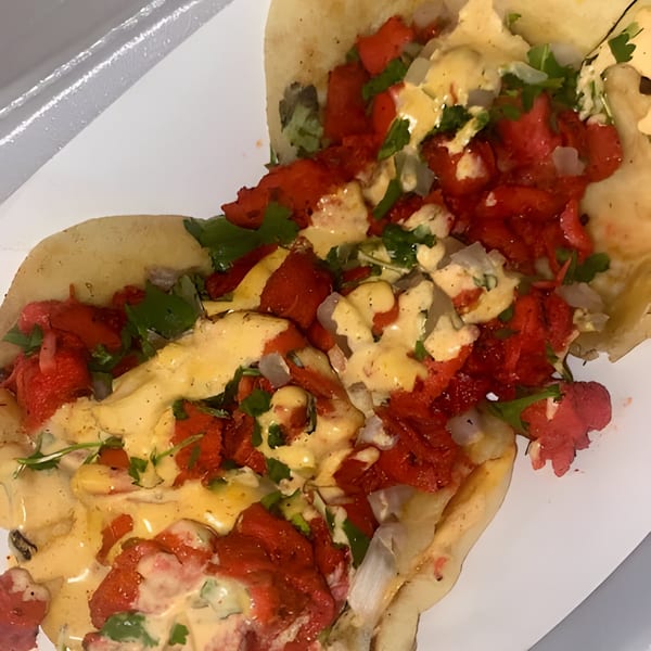 Two Halal Fusionz chicken tikka tacos with creamy sauce, cilantro, and onions on a white plate.