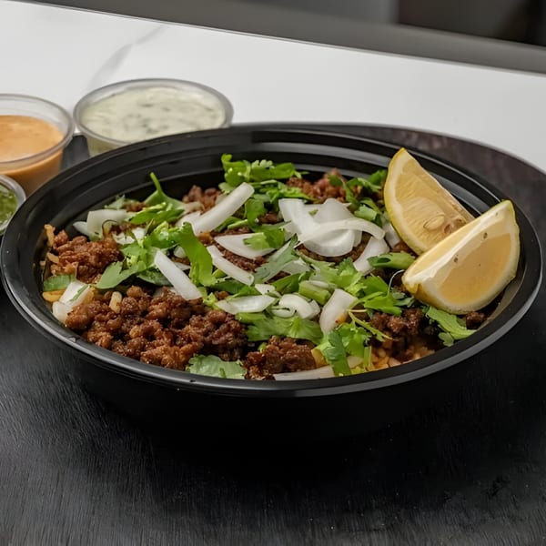 Halal Fusionz's beef and rice bowl with onions, cilantro, and lemon wedges, with sauces.